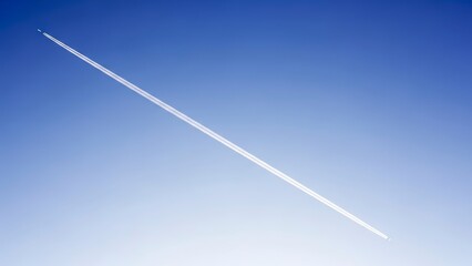 A long white contrail stretches across a clear blue sky.