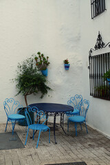 Charming corner with blue wrought iron chairs and table against a whitewashed wall, featuring potted plants that highlight the serene character of this Andalusian setting in Spain