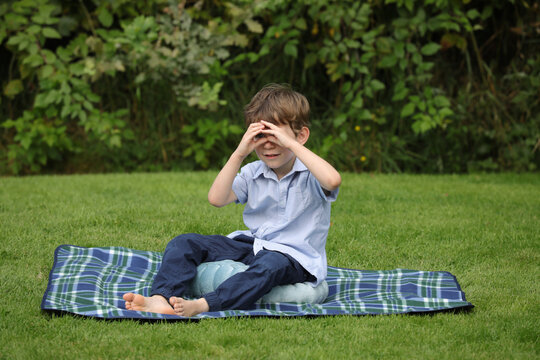 Kleiner, h&uuml;bscher Junge sitzt fr&ouml;hlich auf Decke im Garten