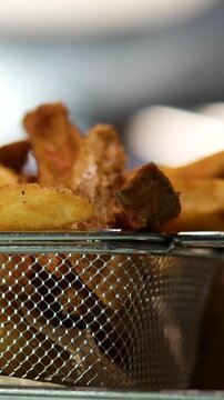 Vast pile of sweet, golden-brown fried ripe plantain slices cooling on a perforated stainless steel tray in commercial kitchen, with metal skimmer nearby