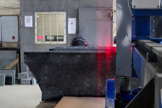 A worker focuses on cutting metal with advanced laser technology in a busy manufacturing plant during daylight hours - Powered by Adobe