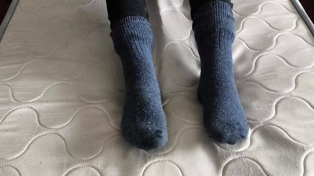 Men's feet in warm woolen socks on the bed. Cold floor in the house concept
