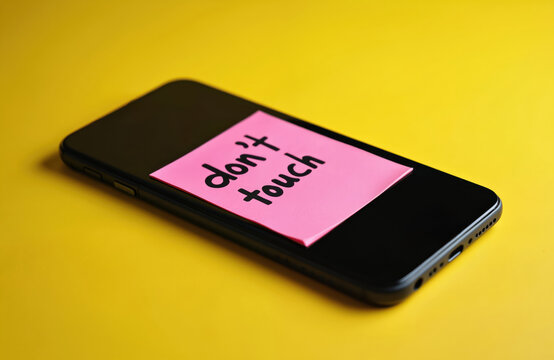 Black smartphone with pink note sticker, inscription dont touch, digital detox concept. Yellow background, focus on phone screen, no gadget use reminder.