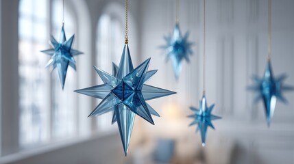 Crystal Blue Star Ornaments Hanging from Gold Strings Against a Bright Blurred White Window Background in a Soft Ambient Lighting