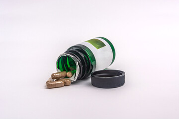 Green pill bottle with herbal capsules spilling out on white background