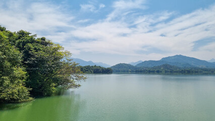 A serene masterpiece captured at Kandalama Lake, where nature's reflection paints a tranquil scene. The still waters mirror lush greenery and a clear blue sky, creating a captivating blend of beauty
