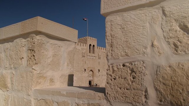Egyptian flag is waving on the top of Qaitbay fort in Alexandria, Egypt. Exterior view of historic stone fortress with massive limestone walls and central citadel tower flying national flag