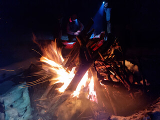 Night campfire in a winter forest. Flames and glowing embers on snow create a contrast of warmth and cold, symbolizing survival, nature connection, and calm during a winter adventure.