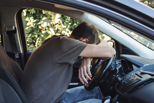 Man sitting inside car with head resting on steering wheel, exhausted male driver experiencing stress or burnout, emotional breakdown during daily routine, transportation and mental health concept