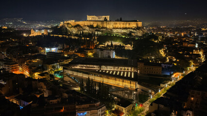 Fototapeta premium Aerial drone night shot of iconic new modern Acropolis museum, Acropolis hill and the Parthenon at the background, Athens historic centre, Attica, Greece
