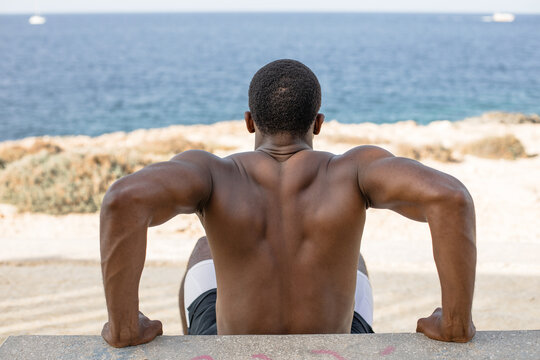 Man doing push-ups on bench outdoors. Athletic man performing incline push-up exercise on a concrete bench during outdoor workout by the sea.