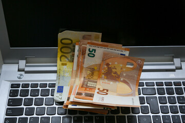 A stack of Euro banknotes of varying denominations, 200 and 50, piled on top of a laptop. Digital economy concept