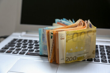 A stack of Euro banknotes of varying denominations, 200 and 50, piled on top of a laptop. Digital economy concept