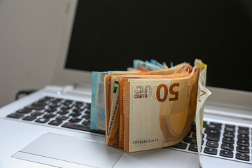 A stack of Euro banknotes of varying denominations, 200 and 50, piled on top of a laptop. Digital economy concept