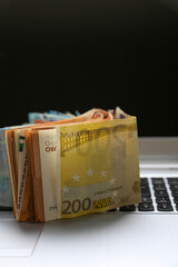 A stack of Euro banknotes of varying denominations, 200 and 50, piled on top of a laptop. Digital economy concept