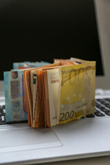 A stack of Euro banknotes of varying denominations, 200 and 50, piled on top of a laptop. Digital economy concept