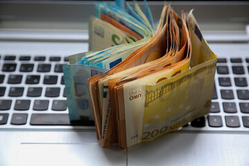 A stack of Euro banknotes of varying denominations, 200 and 50, piled on top of a laptop. Digital economy concept