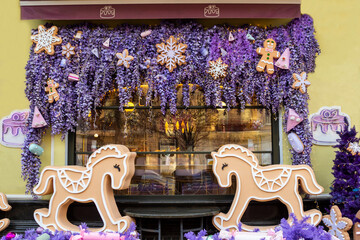 The cafe window is decorated with lilac garlands. Two decorative horses stand in front of the window.