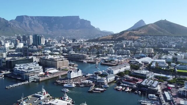 Aerial drone view of the famous V&A Waterfront harbor and marina in Cape Town, South Africa, featuring luxury yachts, city architecture and the iconic Table Mountain landmark on a sunny summer day