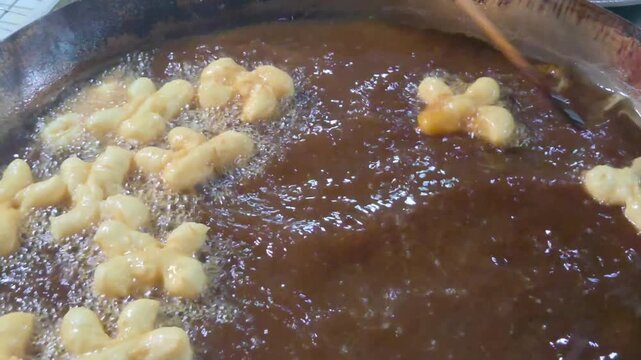 Close-up view of Thai-style Chinese-style fried dough (youtiao or patongo) being fried in a large wok of hot oil. 