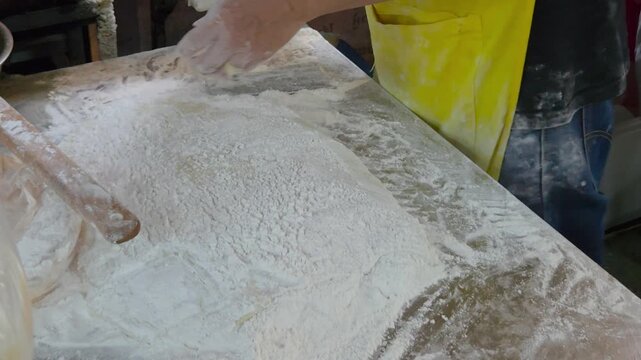 initial stage of making Patongko (deep-fried dough), where a vendor's flour-covered hands work with raw dough on a metal surface heavily dusted with white flour.