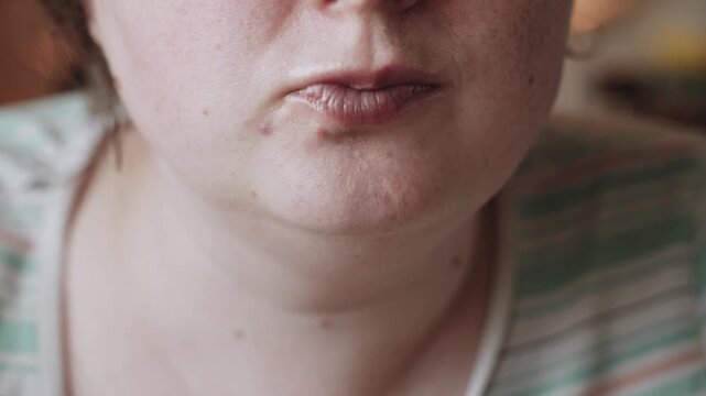 Close-up of Caucasian woman with freckles chewing and eating. Candid overweight woman eats with fork in home kitchen.