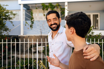 Father places his hand on his teenage son's shoulder while talking outdoors, expressing emotional...