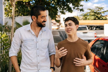 Teenage son speaks while his father listens attentively during an outdoor walk, highlighting active...