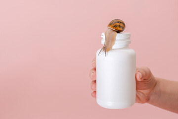 Woman's hand holding bottle for vitamins, beauty capsule, supplements with snail on it. Mockup for brand. Skin care product, spa, luxury, natural beauty © Antonio