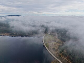 misty waters with distant woods, serene morning with low clouds and muted colors surrounding calm dam