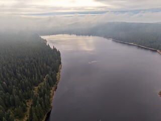 hazy water near mountains, veiled water surface reflecting distant mountain peaks amid thick fog