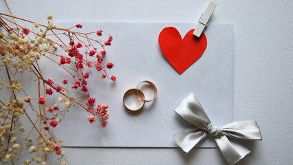 Wedding rings on white card with red paper heart, ribbon and dried flowers, romantic marriage concept