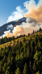 Smoky mountain ridge with green trees burning under clear blue sky with billowing smoke