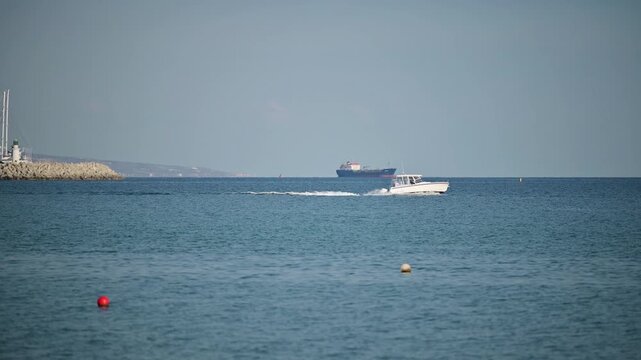 Small motorboat cruising on calm sea with cargo ship in the background, The entrance of the new Limassol Marina