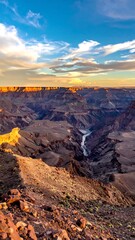A deep canyon with a river snakes through the arid, rocky landscape under a beautiful, colorful sky