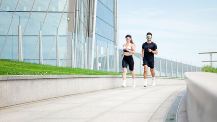 Couple jogging near modern building in urban setting