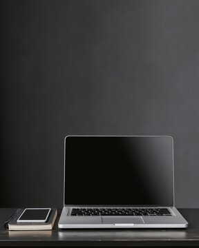 Workspace setup with a laptop, notebook, and smartphone on a black table near a dark wall