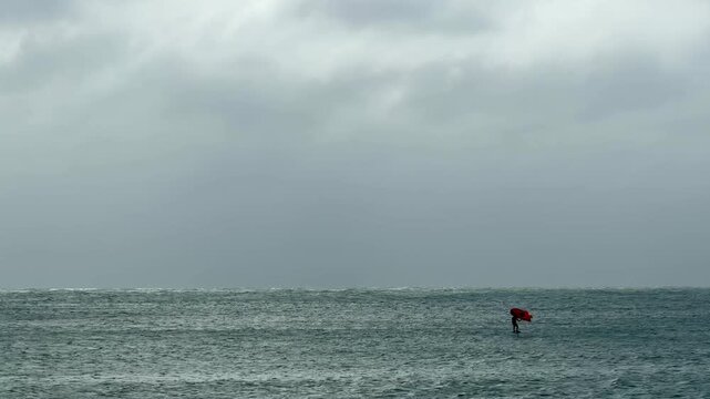 Minimal wide shot of a wing foiler riding smoothly across a calm ocean from right to left under an overcast sky. Clean natural background with copy space, ideal for branding, lifestyle, freedom and tr