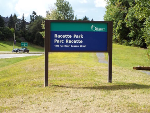 Orleans, ON, Canada-July 2, 2025:A standard green and blue City of Ottawa park sign identifies "Racette Park " located at 1410 rue Henri Lauzon Street.