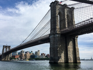 Obraz premium Brooklyn Bridge spanning the East River in New York City, viewed from the waterfront with city skyline.