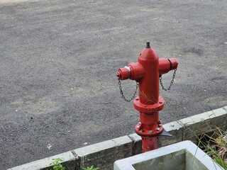 Red fire hydrant standing beside asphalt road and concrete curb in urban outdoor setting