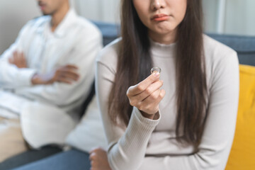 Stressed asian young couple man, woman quarrel on couch, relationship in trouble. Wife hand holding wedding ring in disappointment and upset her husband, which may lead to divorce. Problem of family.