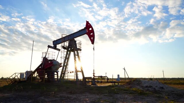 Crude pump jack on sunrise in oil field. Oil Pump Jack Operates on Beautiful Sunset at Oil Field in Industrial Area. Oil drill rig, drilling derrick in oilfield. Crude petroleum industry. 