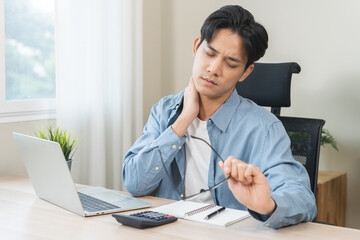 Body muscles stiff problem, ache asian young man pain neck and shoulder while sitting work on chair at home, male holding massaging rubbing, hurt or sore body. Healthcare people, office syndrome.