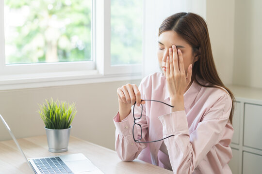 Eye problem concept, fatigue asian young woman tired eyes, irritated rubbing eye dry relief vision pain after work on laptop computer, eye strain, hand holding glasses, suffer migraine, bad blurry.