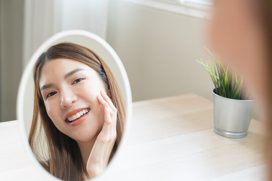 Freshness, nice healthy. Beautiful asian young woman, girl looking on reflection in mirror, hand touching face with makeup cosmetic, skin care routine at home. Happy smile female with natural beauty.