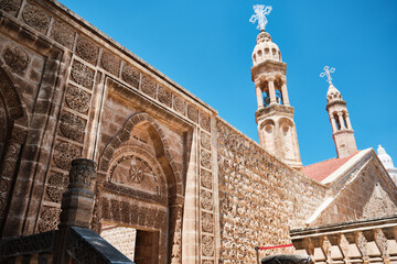 Low-angle view of historic stone church featuring arched entrances and two slender bell towers topped with crosses. Religious orthodox christian architecture at Middle East