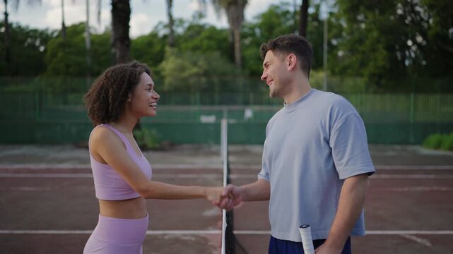 Male and female tennis players shaking hands across court net after game. Outdoor sports scene with friendly atmosphere, mutual respect, active lifestyle and casual tennis match