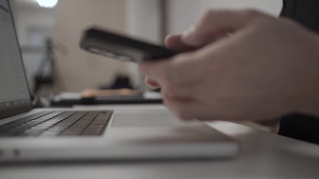 Multitasking Man Browsing Smartphone While Working on Laptop