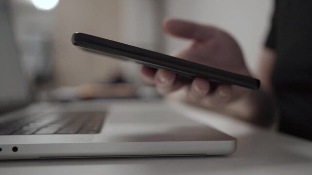 Multitasking Man Browsing Smartphone While Working on Laptop